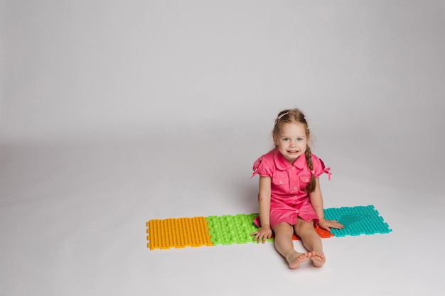 Foto di stock di un bambino che gioca con tamponi di gomma colorati e luminosi per migliorare e sviluppare le capacità motorie sul pavimento. È seduta sulle anche in studio