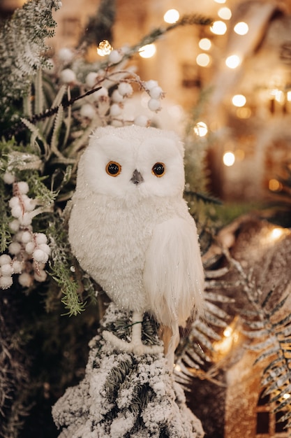 Foto di stock di un bellissimo gufo giocattolo di colore bianco seduto su un ramo di abete con luci bokeh sullo sfondo.