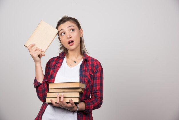 Foto di un giovane studente pensieroso in possesso di una pila di libri.