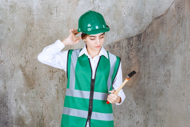 Foto di un'operaia edile con un casco verde che tiene in mano un martello