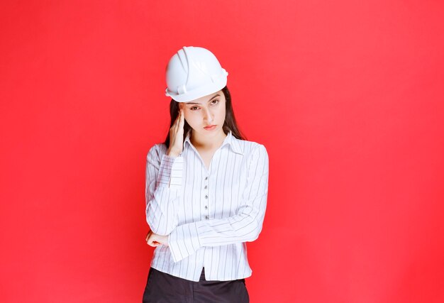 Foto di una bella donna d'affari che indossa un cappello di sicurezza in piedi contro il muro rosso.