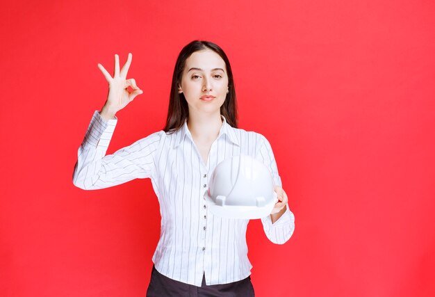 Foto di una bella donna d'affari che tiene il cappello di sicurezza e mostra il gesto giusto.