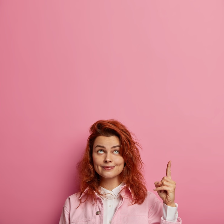 Foto gratuito foto di una bella ragazza, guarda e indica in alto, dà consigli o si mostra verso l'alto, ha un sorriso tenero, una pelle sana