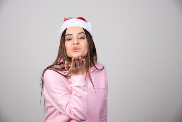 Foto di una bella signora con il cappello di Babbo Natale che invia un bacio d'aria a palmo aperto