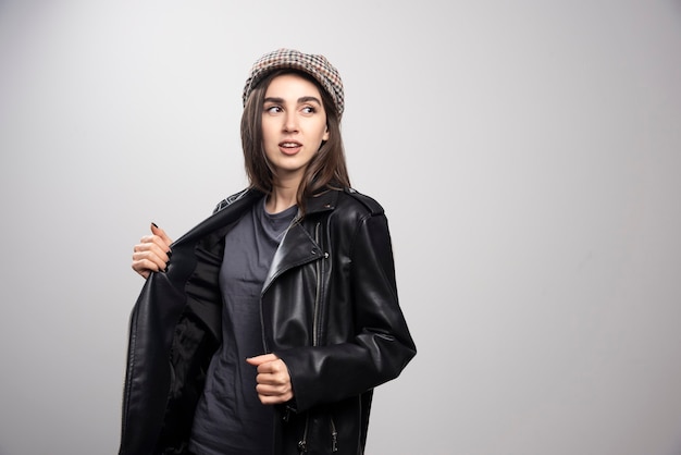 Foto di una donna che guarda lontano in giacca di pelle nera e berretto.