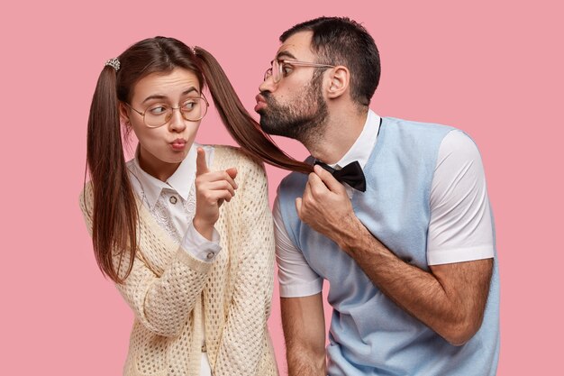 Foto di una donna nerd con due code di cavallo, indossa grandi occhiali, si rifiuta di ricevere il bacio dal compagno di classe
