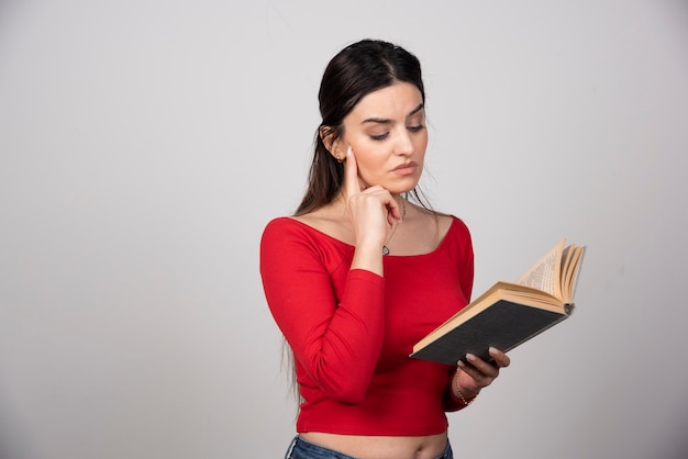 Foto di una donna seria che legge un libro e tiene una matita.