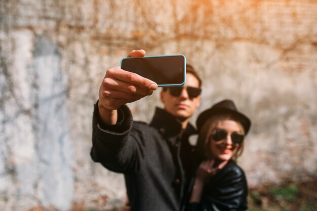 Foto di una giovane bella coppia che fa selfie sul muro grigio