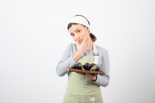 Foto di una giovane cuoca che tiene in mano un piatto di melanzane e pensa