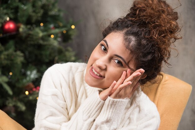 Foto di una giovane donna seduta su una sedia comoda vicino all'albero di Natale