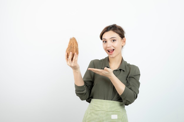 Foto di una giovane ragazza che tiene una noce di cocco pelosa su bianco. Foto di alta qualità