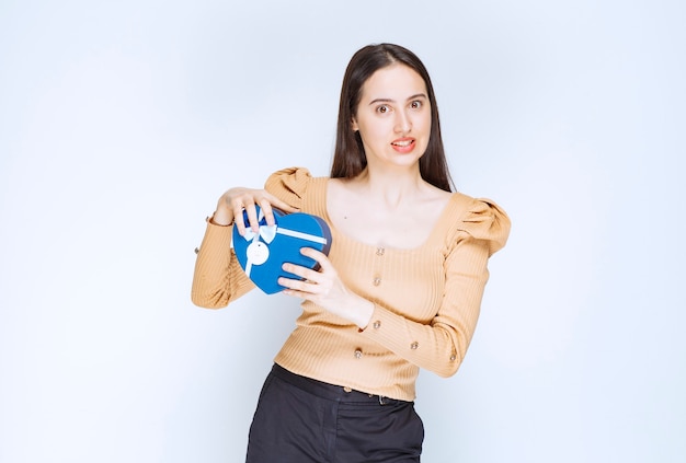 Foto di una modella di giovane donna che tiene una confezione regalo blu contro il muro bianco.