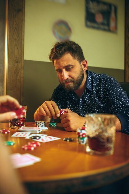 Foto di vista laterale degli amici che si siedono alla tavola di legno. Amici che si divertono mentre giocano a gioco da tavolo.