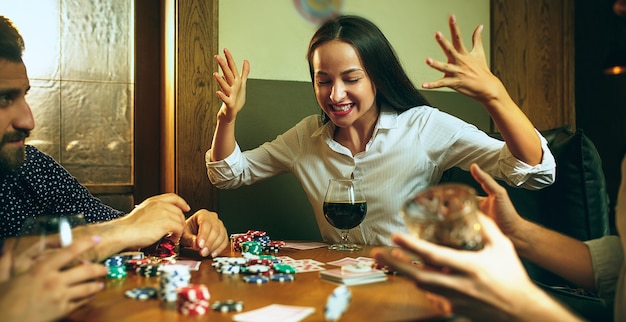 Foto di vista laterale degli amici che si siedono alla tavola di legno. Amici che si divertono mentre giocano a gioco da tavolo.