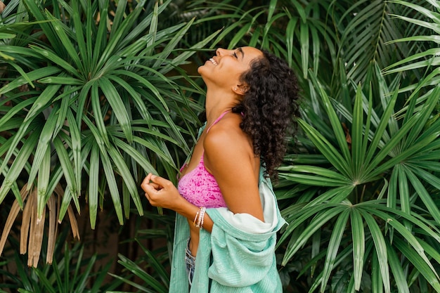 Foto estiva di donna bruna con i capelli ricci in posa su foglie tropicali