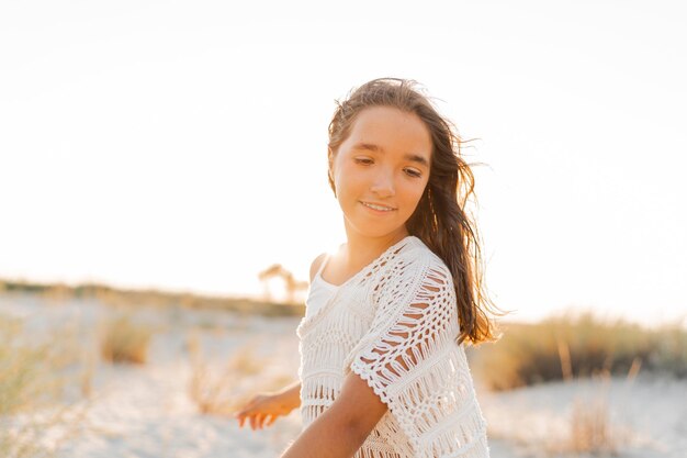 Foto estiva di una piccola ragazza in un elegante abito boho in posa sulla spiaggia Colori caldi del tramonto Concetto di viaggio e wacation