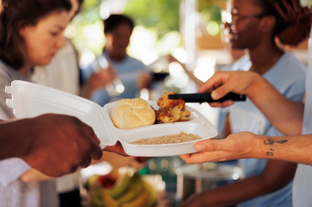 Foto focalizzata su un uomo caucasico che serve pane, pollo e fagioli al forno a una persona afroamericana povera e affamata in una raccolta alimentare senza scopo di lucro.