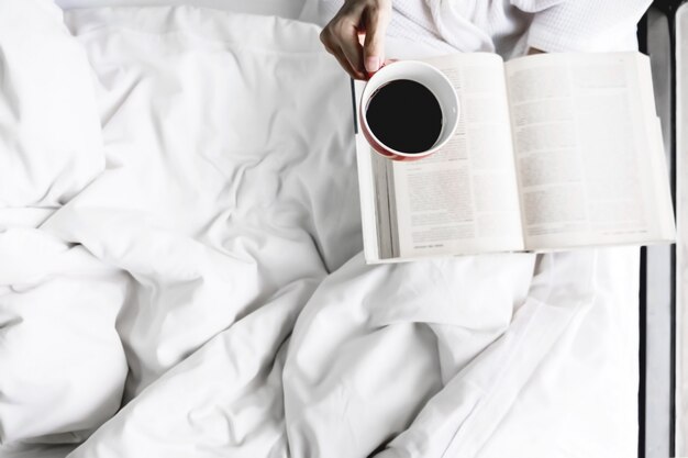 Foto morbida di donna sul letto con vecchio libro e tazza di caffè e copia spazio.