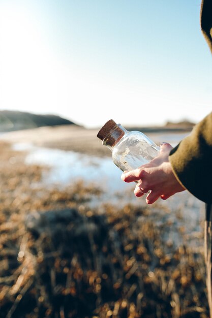 Foto poco profonda del fuoco della persona che tiene la bottiglia di vetro trasparente