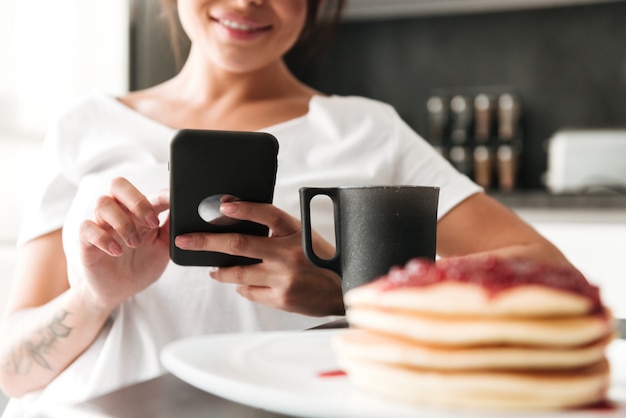 Foto potata della giovane donna allegra che per mezzo del telefono cellulare