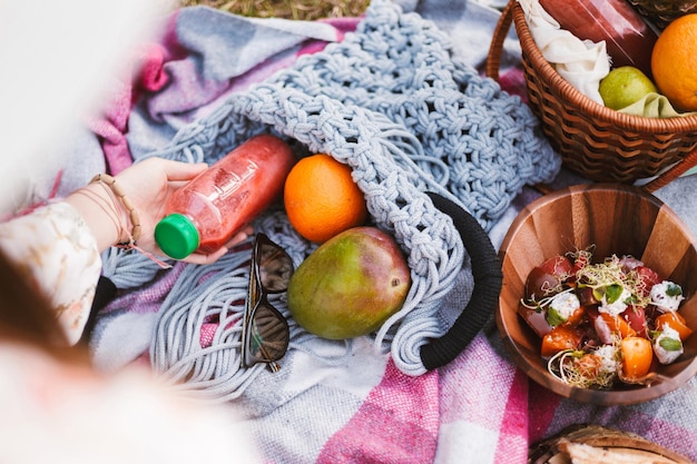 Foto ravvicinata della borsa blu con bottiglia di succo e frutta sulla coperta da picnic. Cibo delizioso durante il picnic nel parco