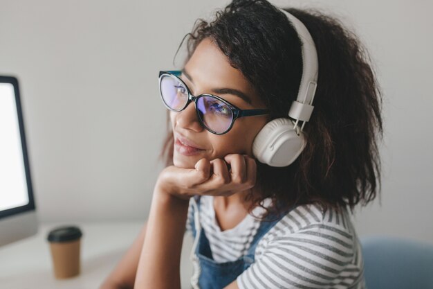 Foto ravvicinata di una ragazza sognante con la pelle marrone chiaro che pensa a qualcosa di piacevole mentre si ascolta la musica