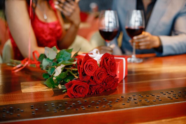 Foto ritagliata di rose rosse e confezione regalo su un tavolo in ristorante