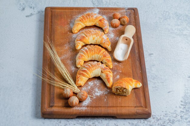 Foto verticale di croissant freschi fatti in casa su tavola di legno su superficie grigia.