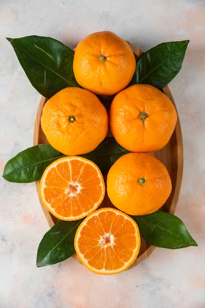 Foto verticale di mandarini clementine interi o tagliati a metà sul piatto di legno. Avvicinamento