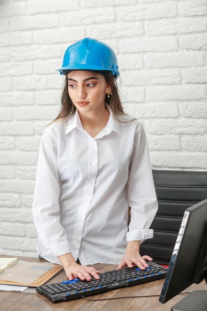 Foto verticale di una giovane donna che indossa un casco da costruzione e lavora al pc