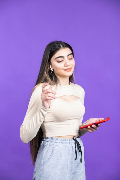 Foto verticale di una giovane donna che tiene il telefono e ascolta musica con le cuffie