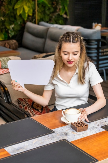 Foto verticale di una giovane donna che tiene in mano un'idea bianca e guarda il suo caffè