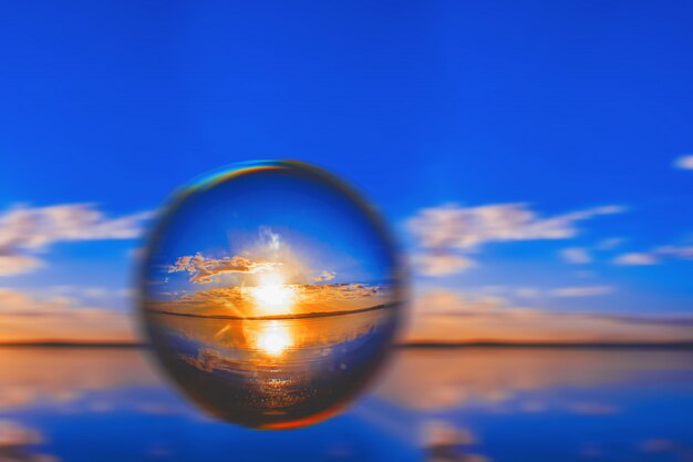 Fotografia creativa della palla dell'obiettivo della luce solare sull'orizzonte con le nuvole intorno nel cielo blu