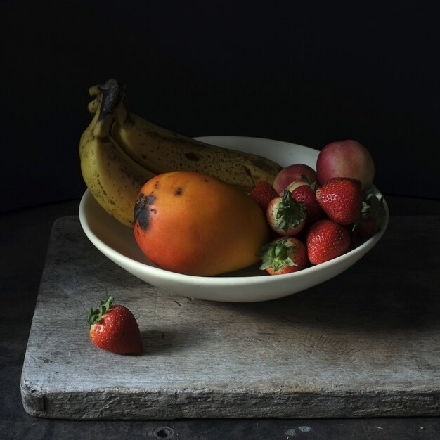 Fotografia di natura morta della frutta fresca in un piatto bianco su fondo nero