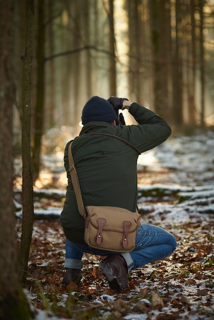 Fotografo che scatta foto in una foresta immersa nel verde ricoperta di neve e foglie