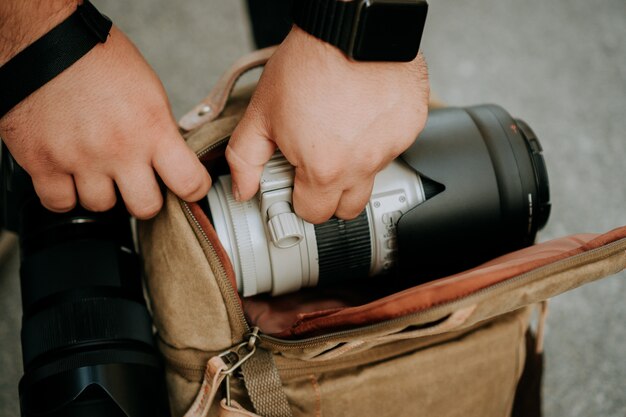Fotografo che tira fuori un obiettivo bianco della fotocamera da una borsa della fotocamera