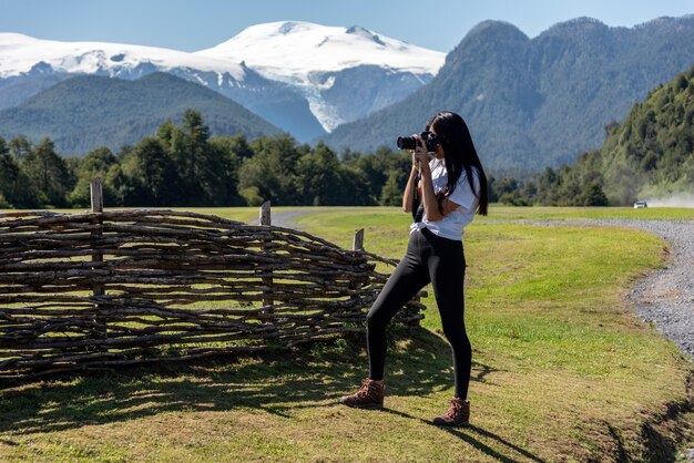 Fotografo con capelli lunghi e camicia bianca che lavora nel campo con le montagne