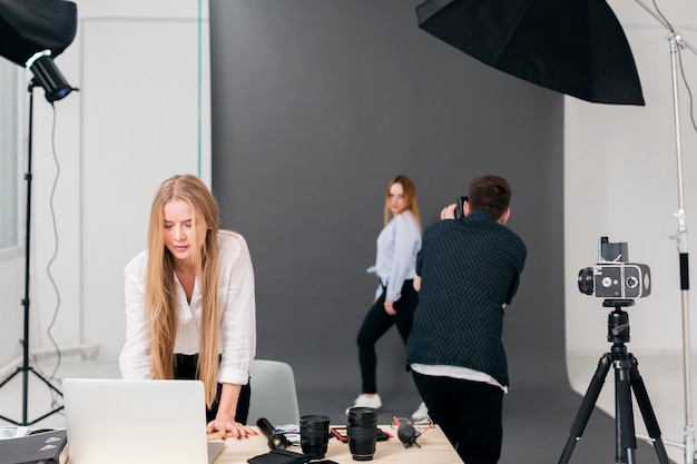 Fotografo con il modello e la donna che lavora al computer portatile dalla vista