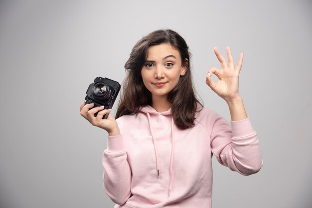 Fotografo femminile che tiene la macchina fotografica e che fa segno giusto.