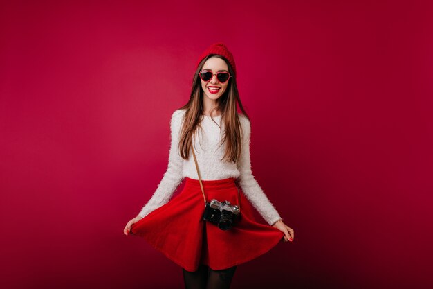 Fotografo femminile dai capelli lunghi entusiasta che gioca con la gonna rossa