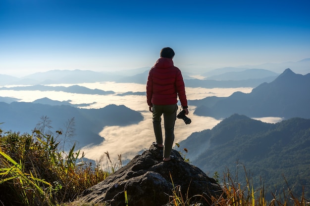 Fotografo mano che tiene la fotocamera e in piedi sulla cima della roccia in natura. Concetto di viaggio.