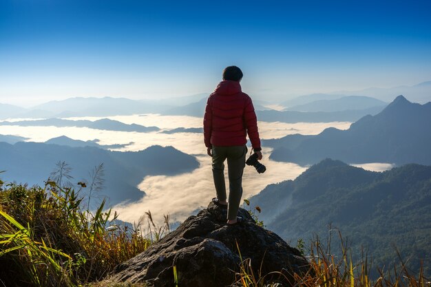 Fotografo mano che tiene la fotocamera e in piedi sulla cima della roccia in natura. Concetto di viaggio.