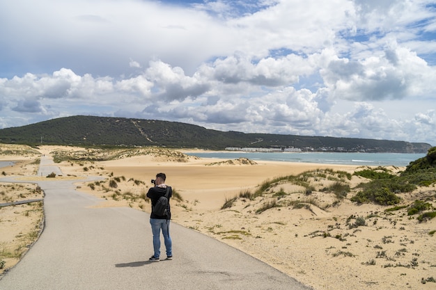 Fotografo maschio che cammina attraverso una spiaggia sotto un cielo nuvoloso durante il giorno in Andalusia, Spagna