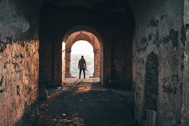 Fotografo maschio che sta nell'arco di vecchia architettura abbandonata