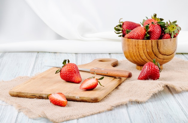 Fragola fresca di vista laterale in un coltello di legno della ciotola e bordo su fondo bianco