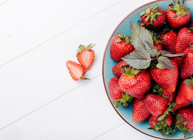 Fragola fresca di vista laterale sulla destra del trhe con lo spazio della copia e del basilico su fondo bianco