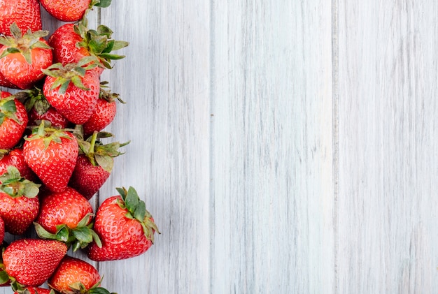 Fragola fresca di vista superiore a sinistra con lo spazio della copia su fondo di legno bianco