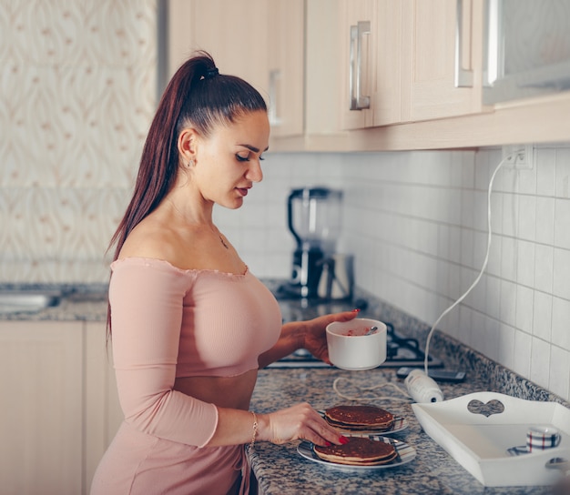 Fragola mescolata di versamento della donna splendida sulle crepes in cucina in cima e pantaloni del raccolto di rosa di color salmone