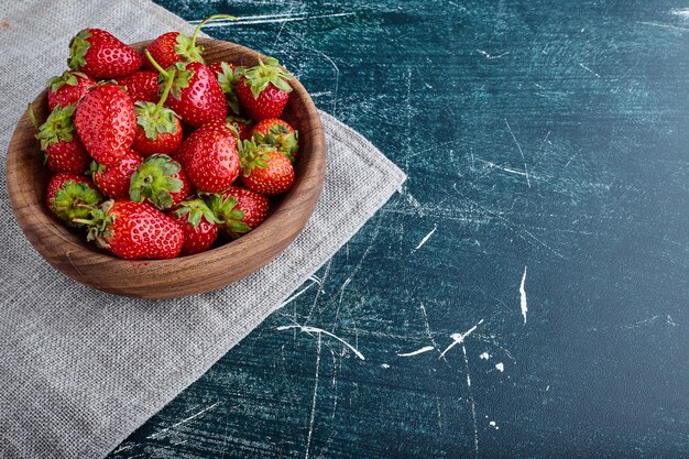 Fragola rossa isolata su sfondo blu in una tazza di legno.