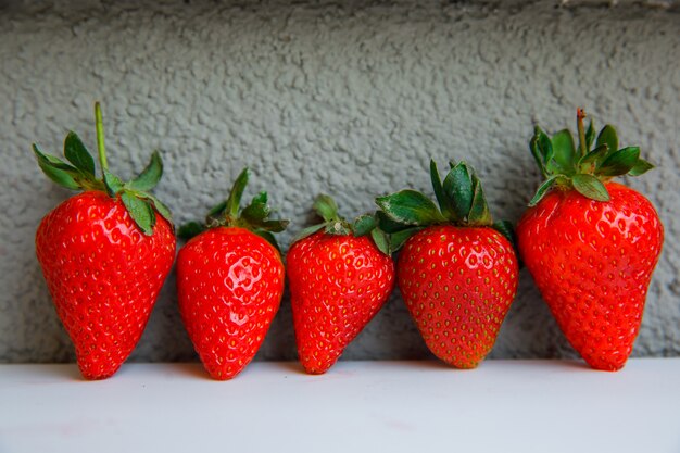 Fragole con le foglie sulla parete grigia dello stucco e bianco, vista laterale.